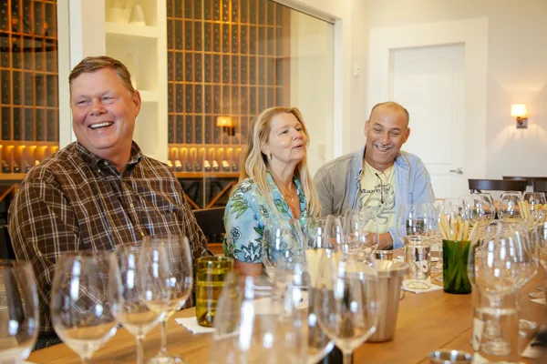 Three people tasting wine at cellar table with bottles and glassware