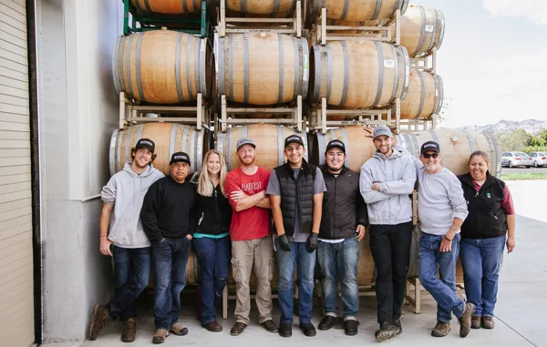 Harvest crew of ten standing in front of stacked wine barrels