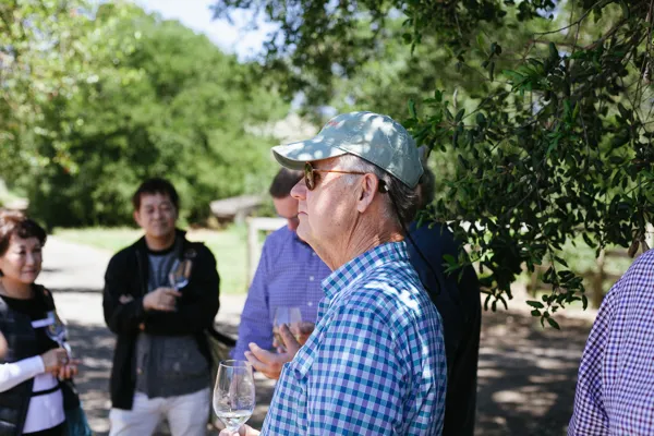Vineyard visit with man in cap discussing grapes with guests