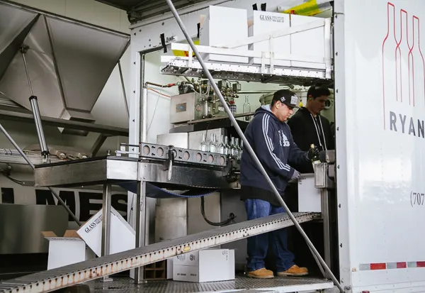 Workers operating bottling line machinery with wine bottles and equipment