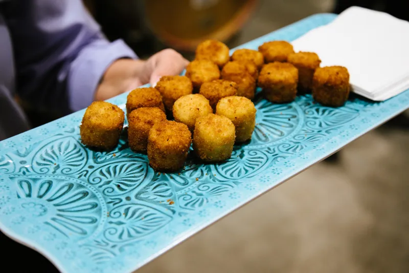 Golden-fried appetizers on decorative teal plate with wine bottle nearby