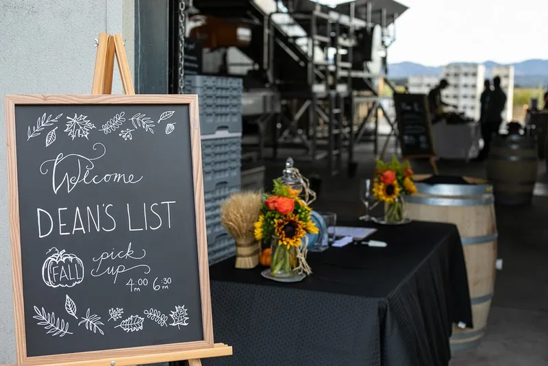Welcome sign for Dean's List event with sunflower arrangement and vineyard backdrop