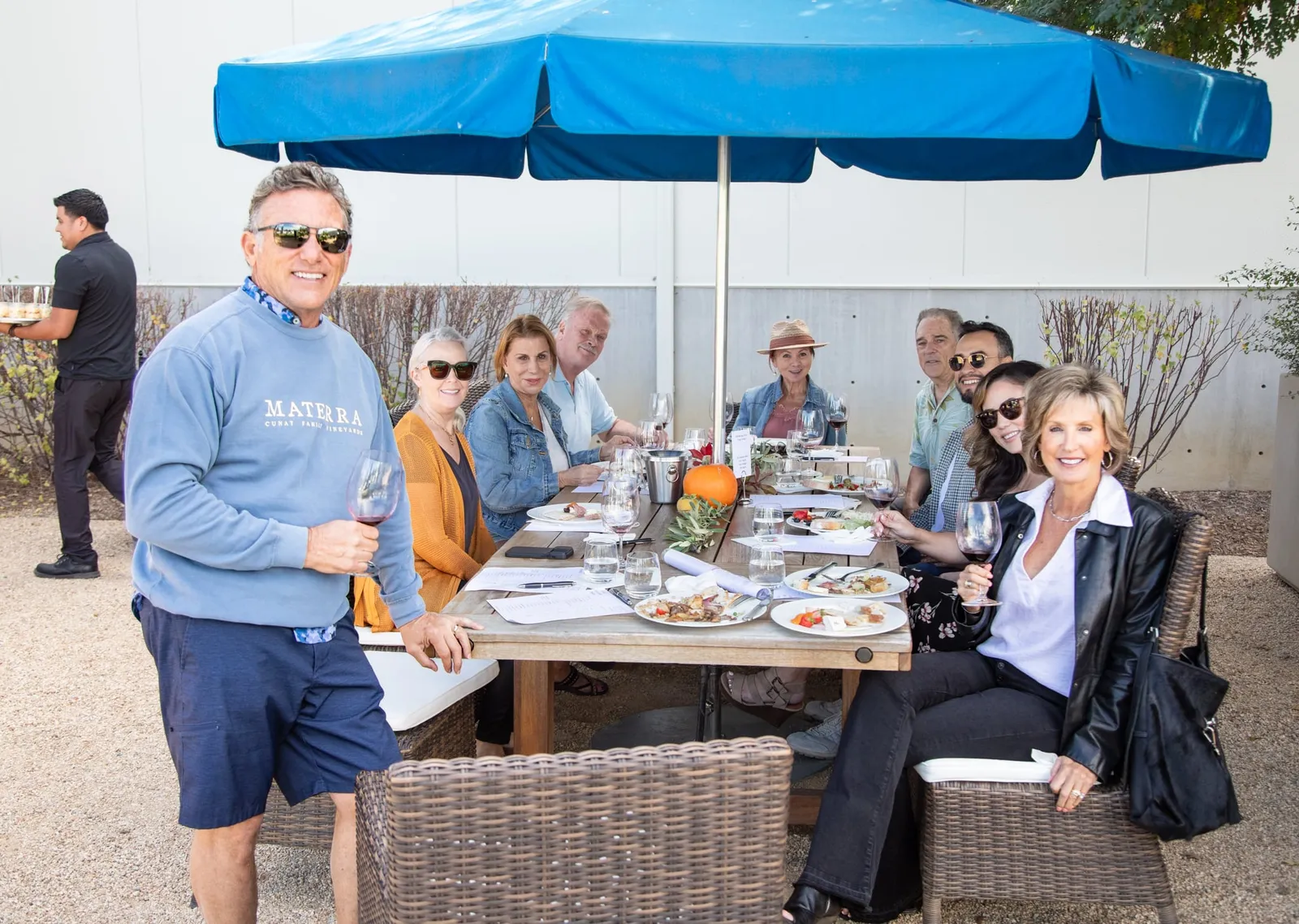 Group dining under blue umbrella on winery grounds