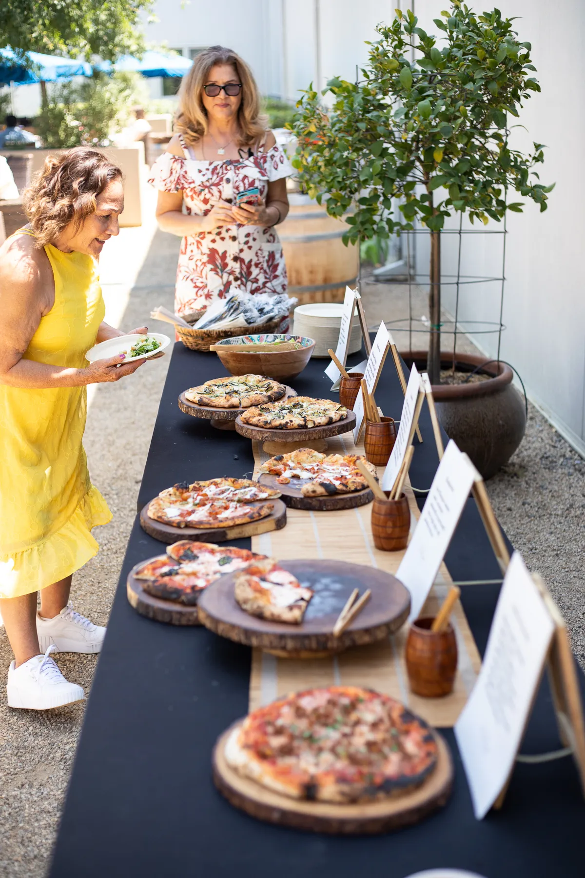 Women serving and sampling pizzas at outdoor summer party table