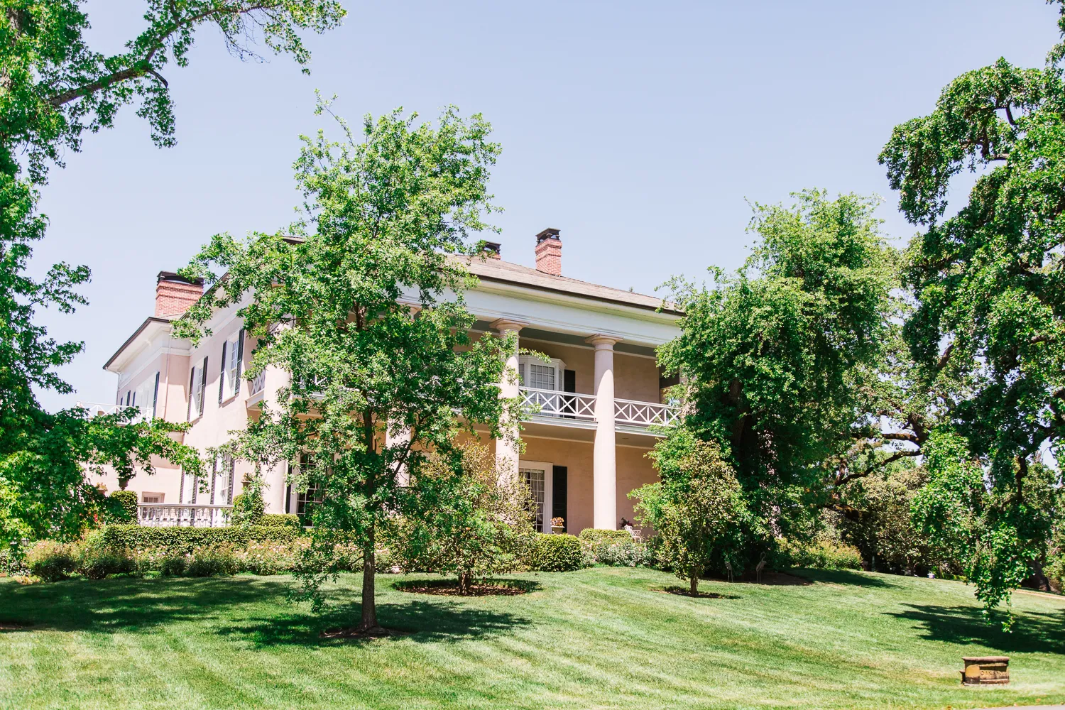 Classical pink mansion with columns surrounded by mature trees