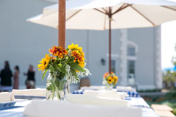 Event table setup with yellow and orange flowers under white umbrellas