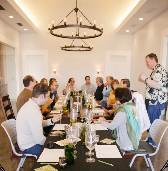 Wine tasting event attendees seated at long table for May blending